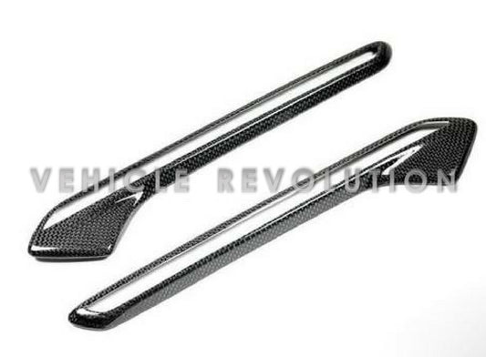 A pair of carbon fiber and ABS fender light trims for BMW vehicles, featuring a gloss black finish and a textured weave design.