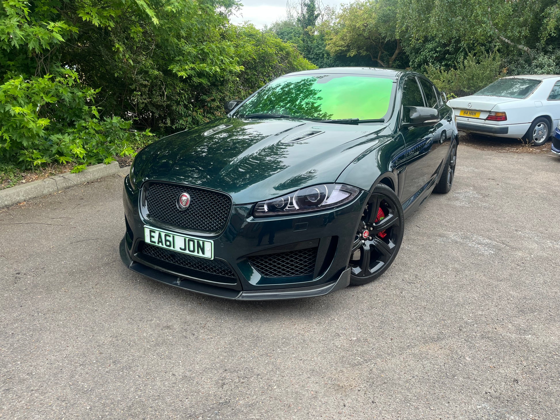 Black Jaguar car parked on a driveway with greenery in the background