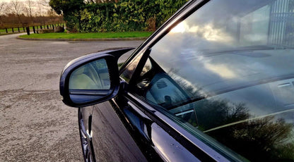 Car side mirror reflecting a cloudy sky and surrounding environment.